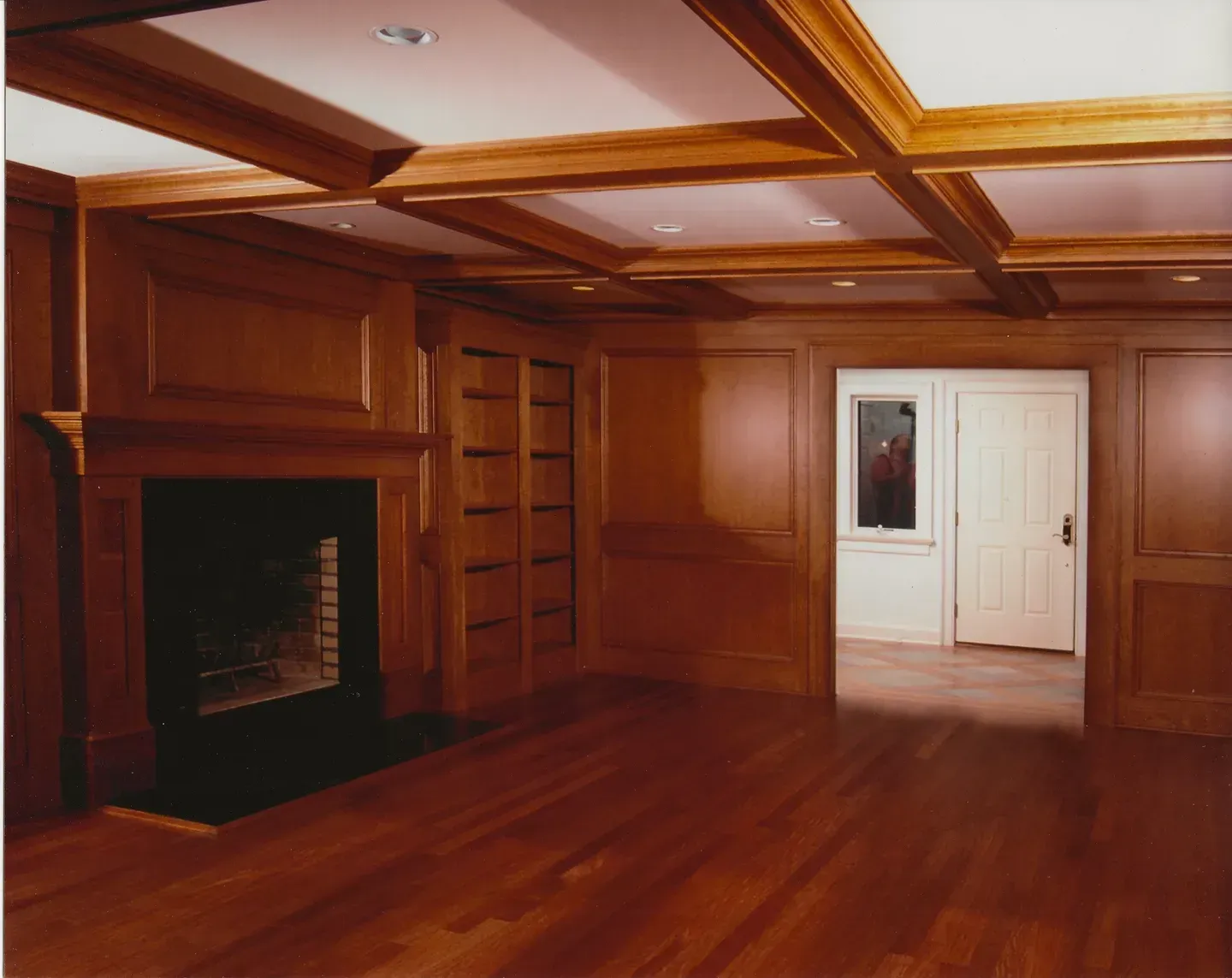 Empty wood-paneled room with a fireplace, coffered ceiling, and double doors.
