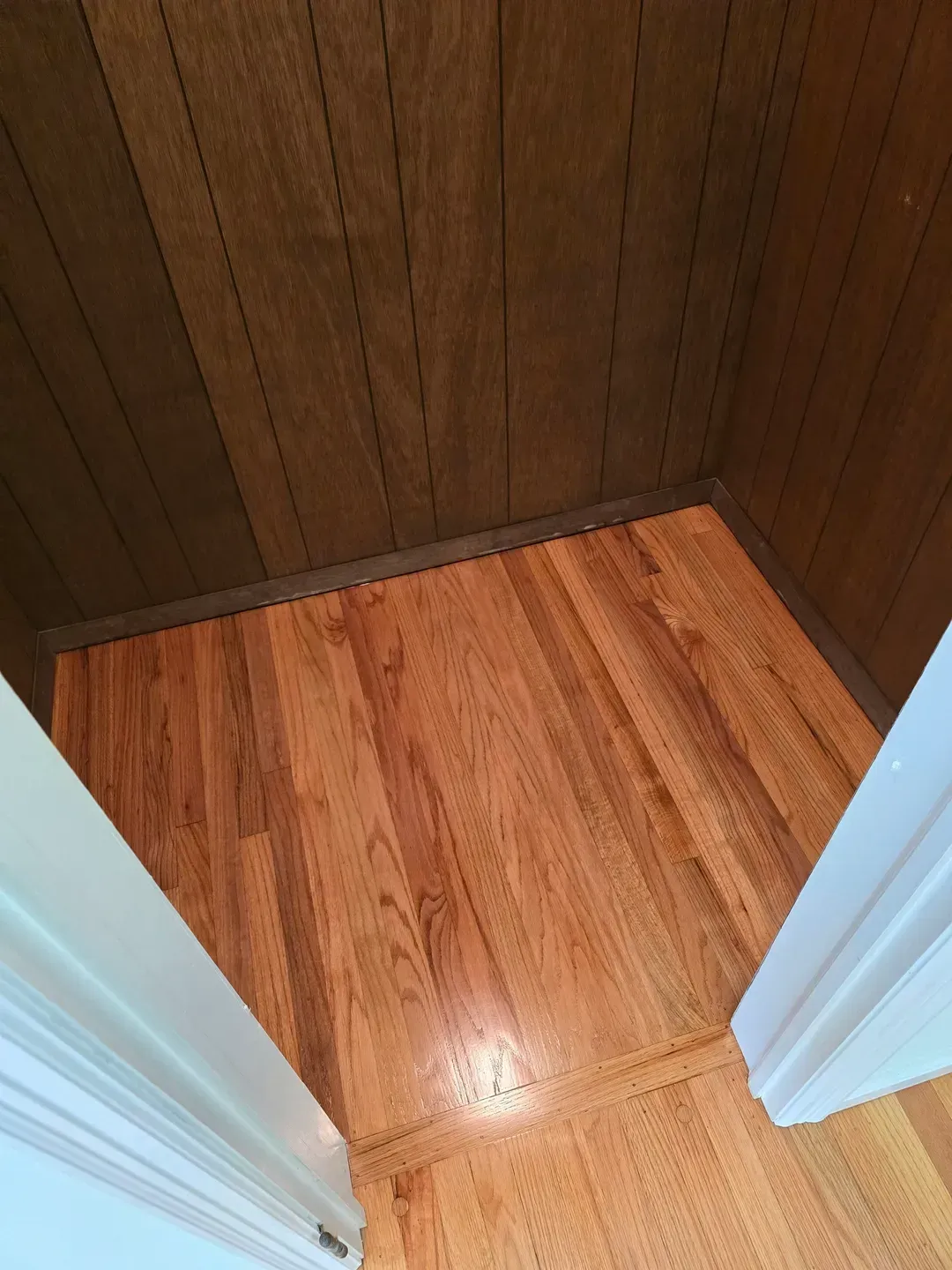 Empty wooden closet with open white doors and wood-paneled walls