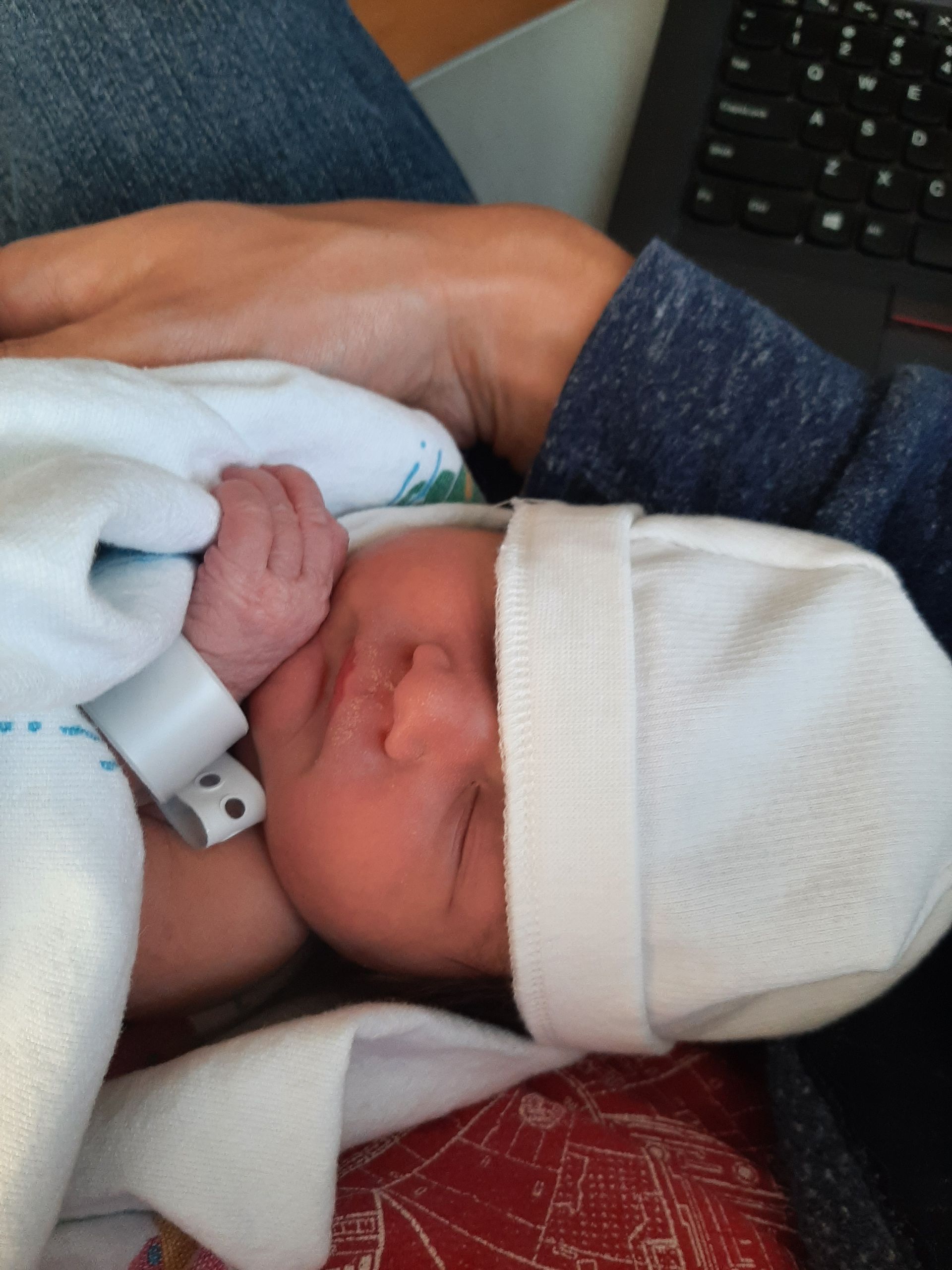 A person is holding a newborn baby wearing a white hat