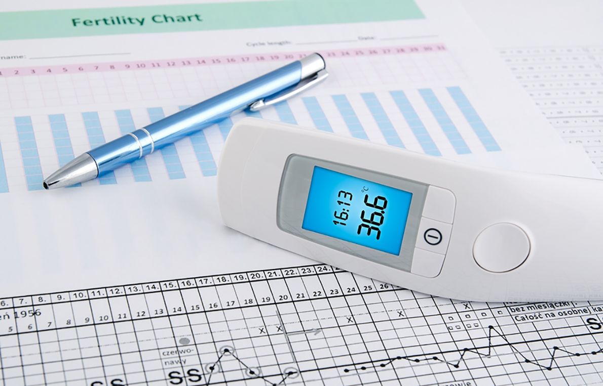 A thermometer is sitting on top of a fertility chart next to a pen.