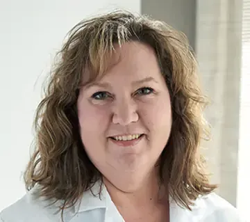 A woman in a white lab coat is smiling for the camera.