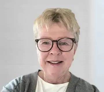 A woman wearing glasses and a gray jacket is smiling for the camera.