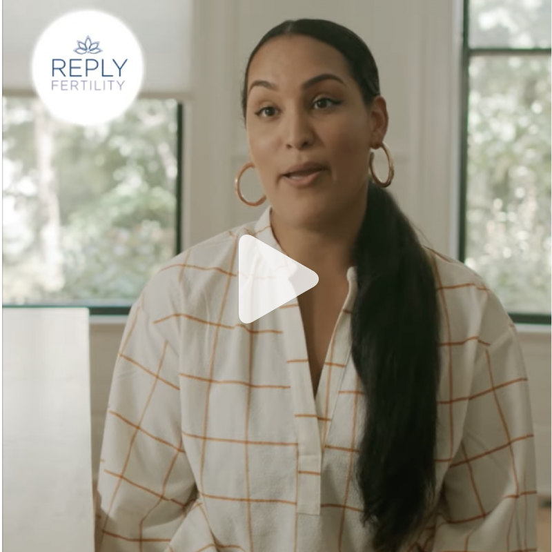 A woman is wearing hoop earrings and a plaid shirt with a reply fertility logo in the background