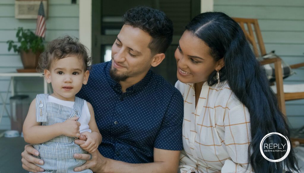 A man and woman are sitting on a porch holding a baby.