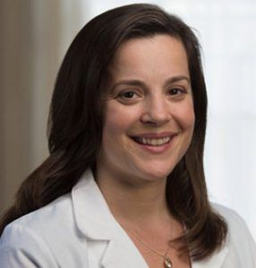 A woman in a white lab coat is smiling for the camera.