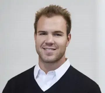 A man wearing a black sweater and a white shirt is smiling for the camera.