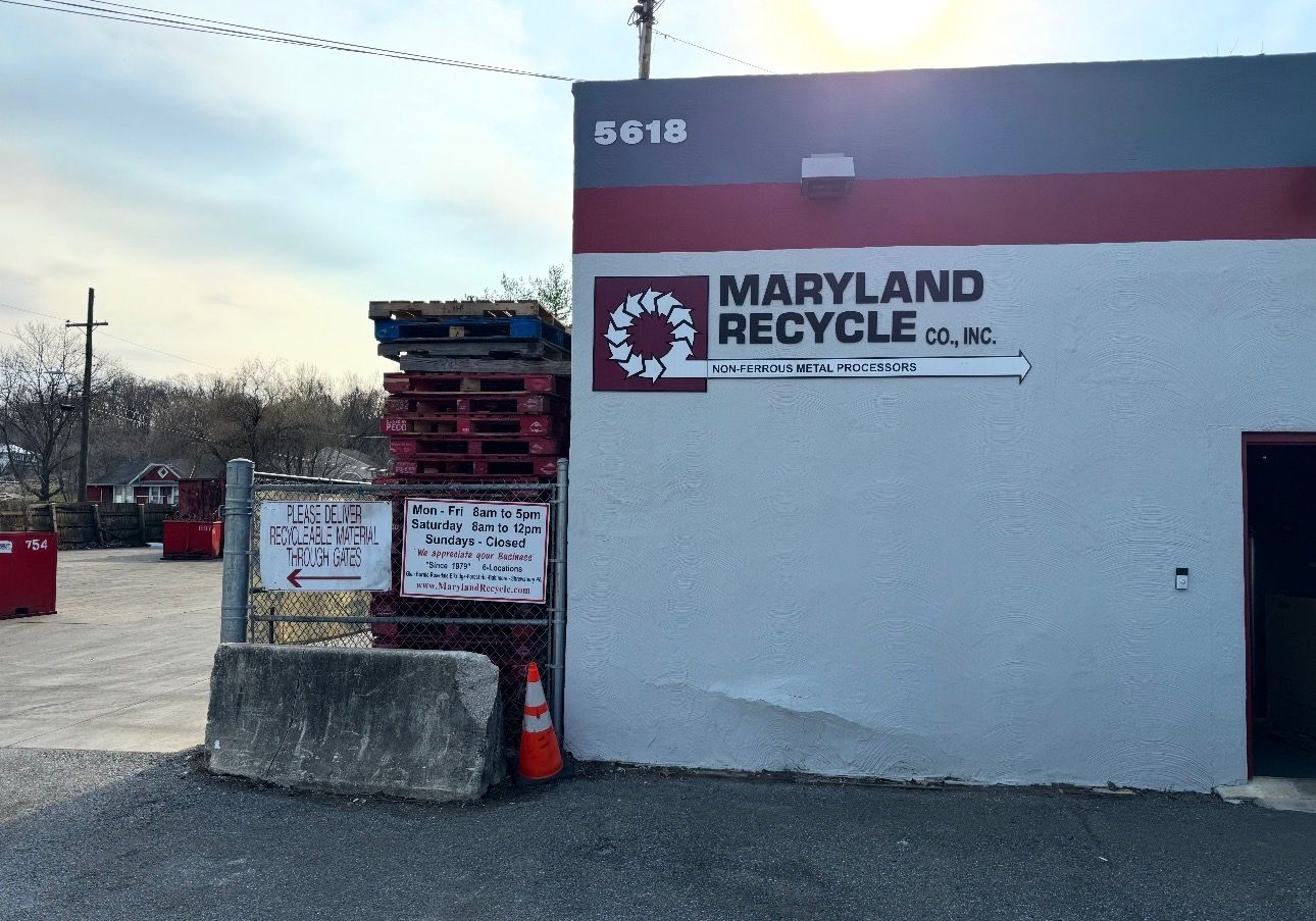 Exterior of Maryland Recycle Co. with a stack of wooden pallets, a concrete barrier, and an orange traffic cone.