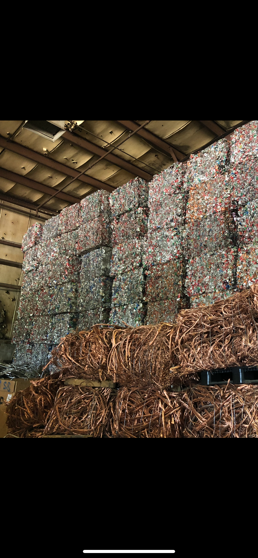 Large stacks of bundled aluminum cans and bales of copper wiring in a warehouse storage facility.
