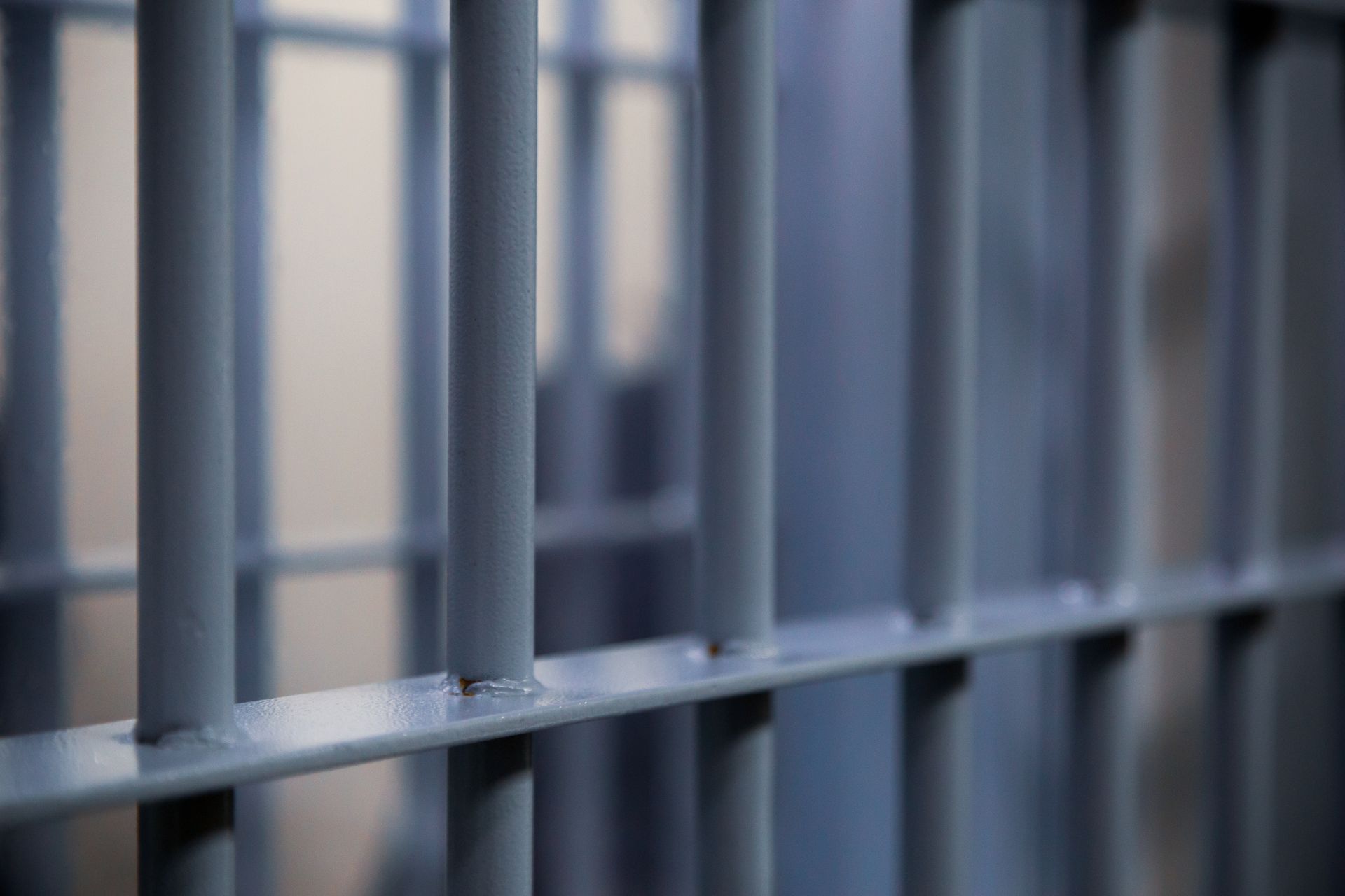 Close-up of gray metal jail cell bars with soft blurred light in the background