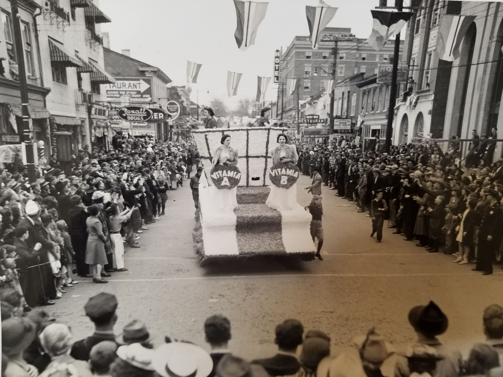 Parade float with people, surrounded by crowds lining a city street with flags.