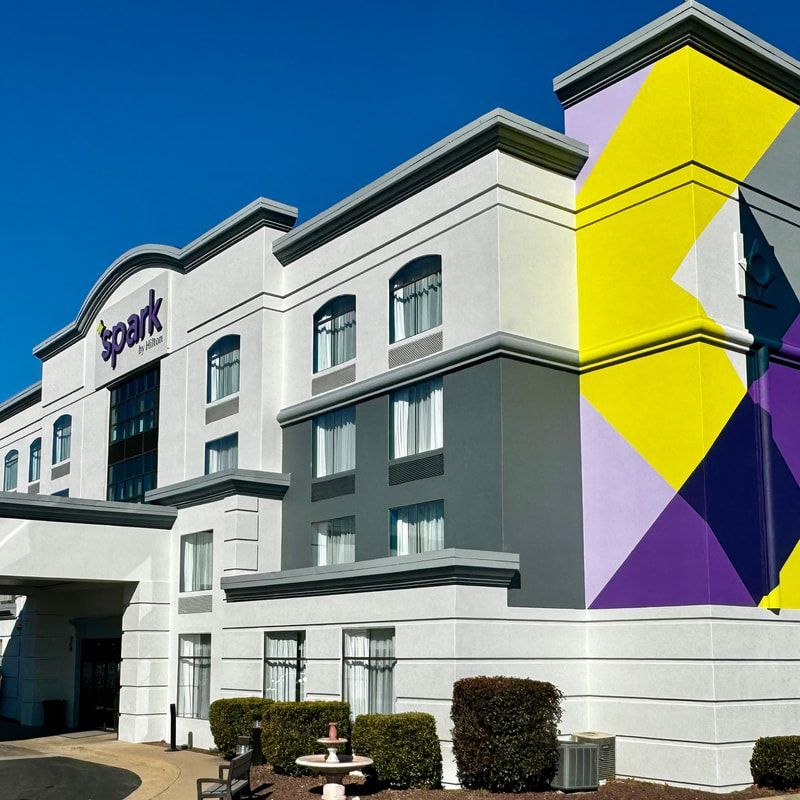 Exterior of Spark by Hilton hotel with colorful geometric mural. White and gray building under blue sky.