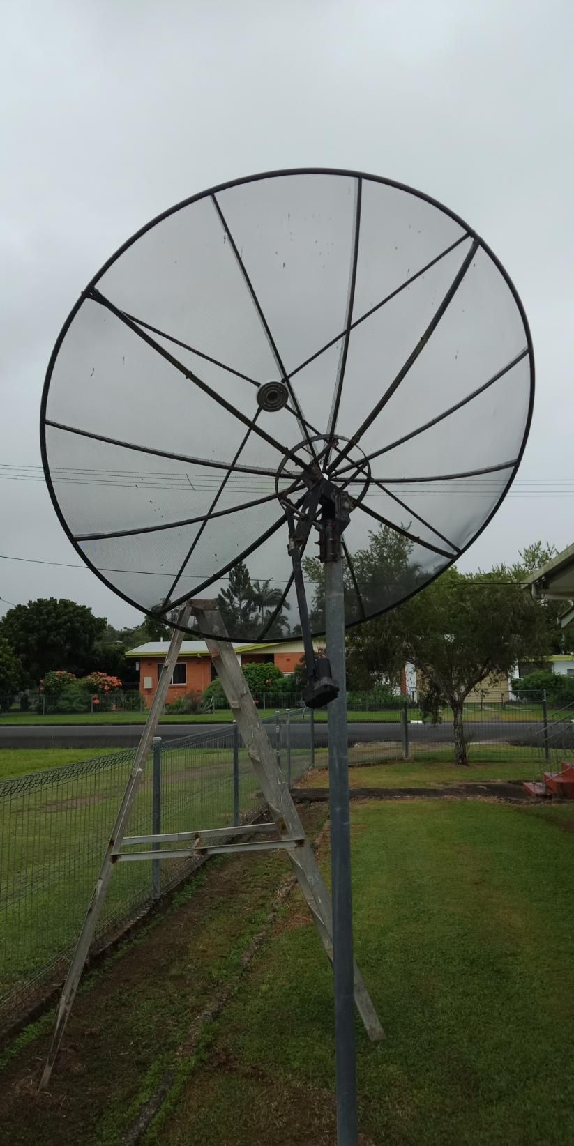 A Large Satellite Dish Is Sitting On Top Of A Metal Pole In A Grassy Field — Laurence Capocchi Antenna Guy In Trinity Beach, QLD