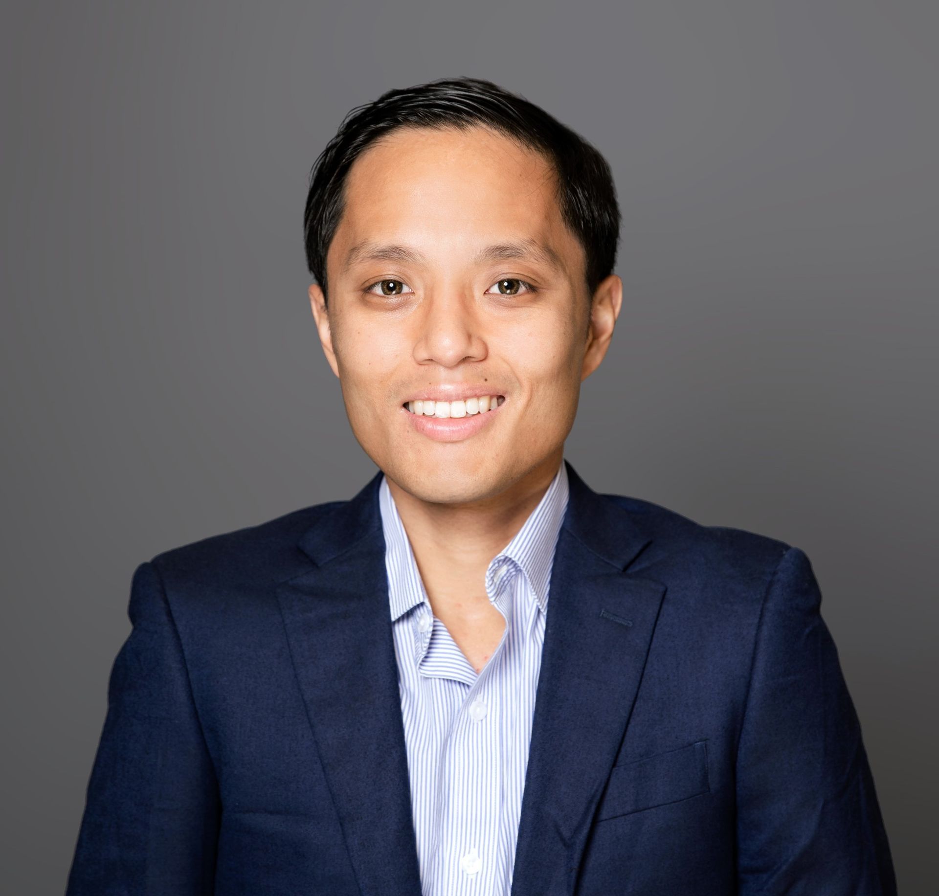 Smiling person in a navy blazer and light blue shirt against a gray background