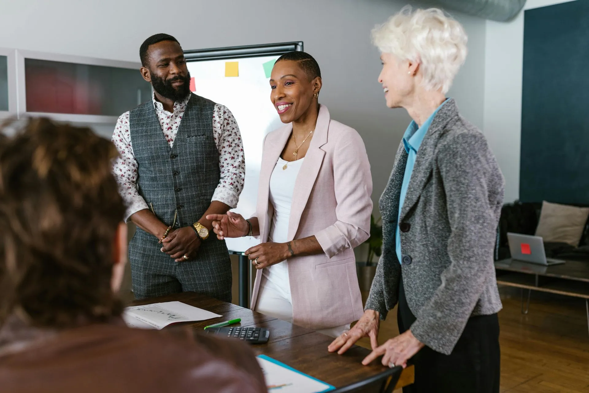 Business colleagues in a meeting, gesturing and talking at a table in a modern office space.