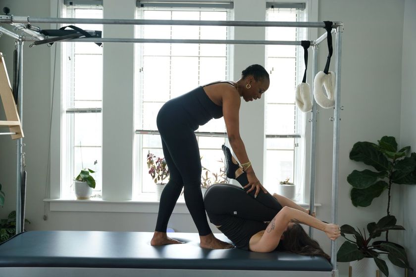 Pilates instructor assisting a client on a reformer in a bright studio