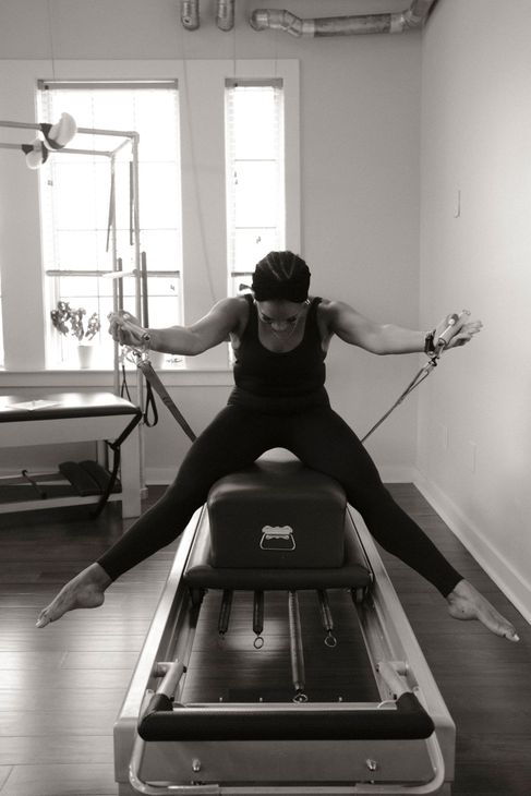 Person stretching on a Pilates reformer machine in a studio, arms and legs extended