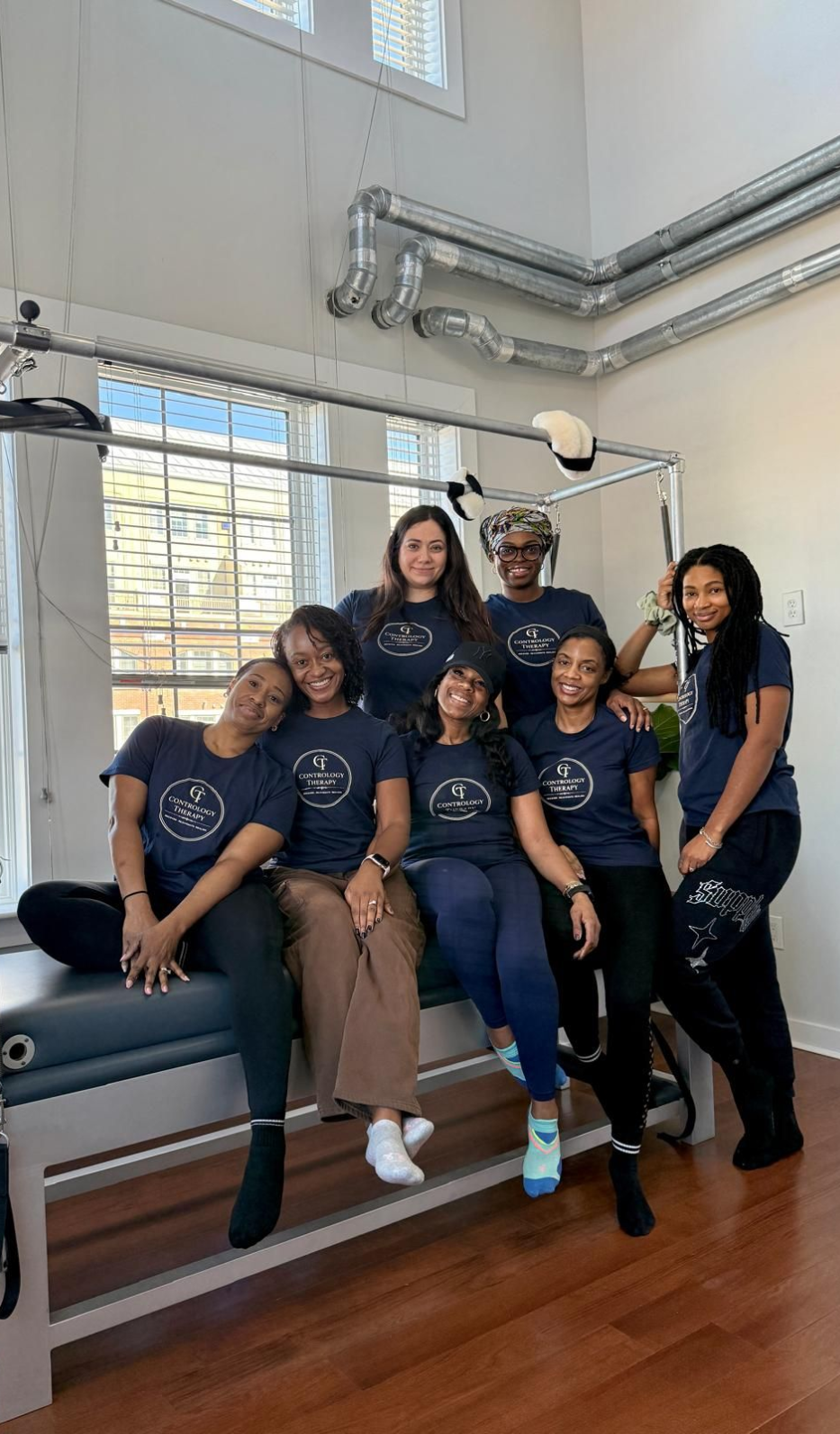 Six people in matching navy shirts pose in a bright indoor with high windows 