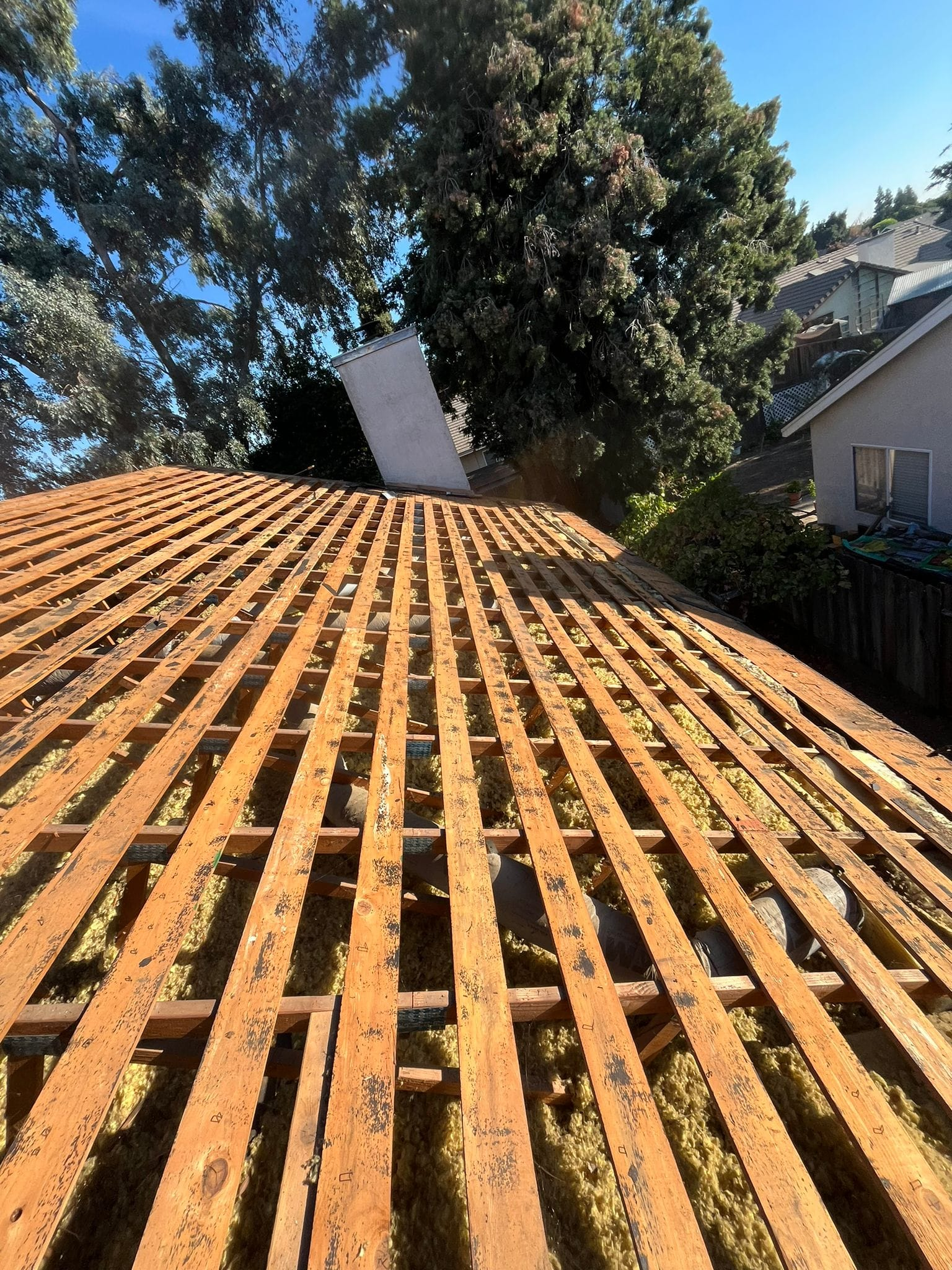 A sloped roof under construction, showing exposed wooden framing and battens with a chimney in the background.
