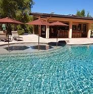 Resort pool with turquoise water, lounge chairs, and red umbrellas beside a patio and building Resort pool with turquoise water, lounge chairs, and red umbrellas beside a patio and building