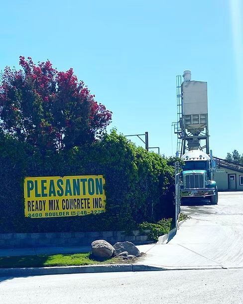 Pleasanton Ready Mix Concrete sign by a driveway with a concrete truck and silo