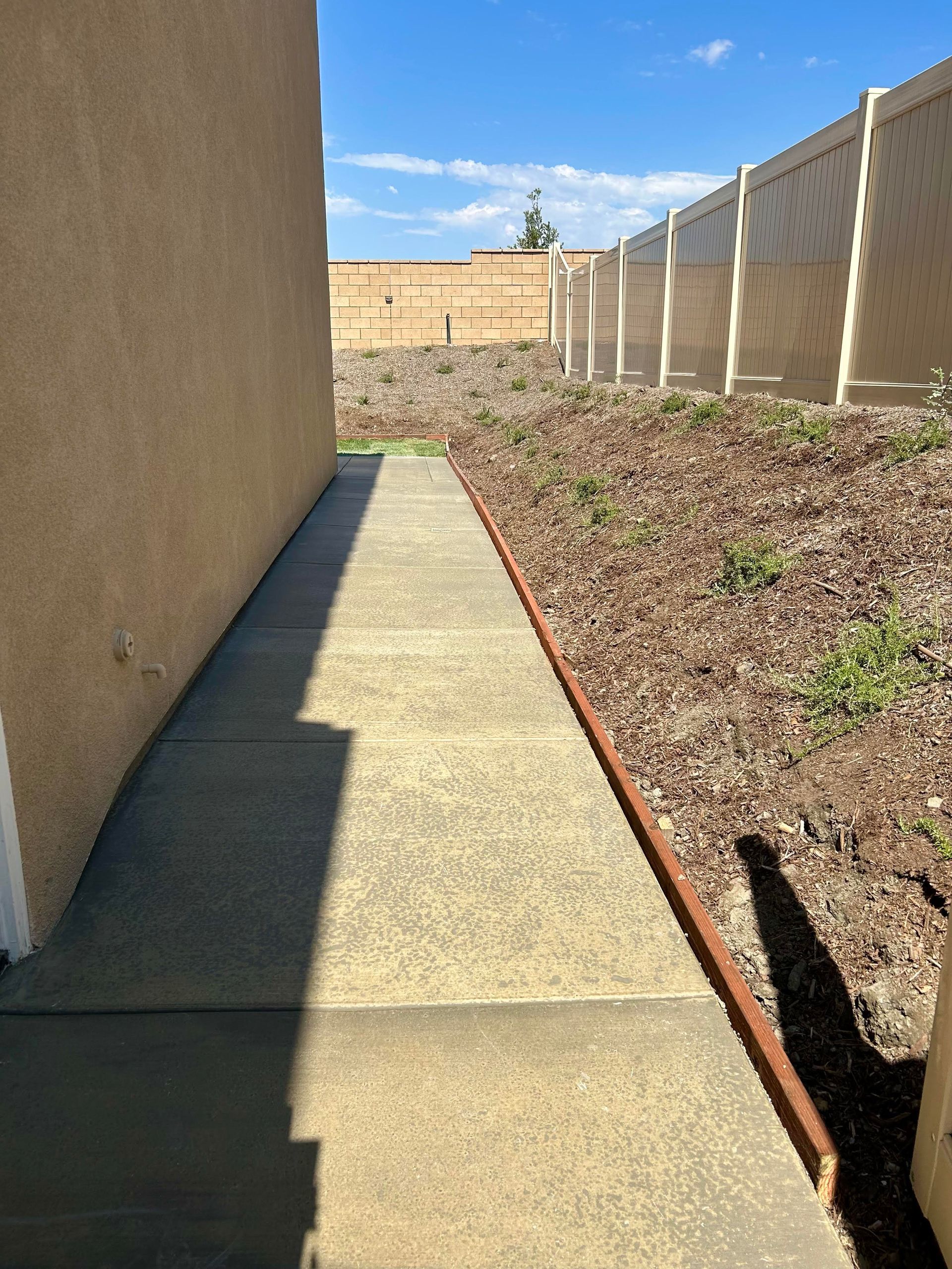 A sidewalk leading to a house with a fence in the background.