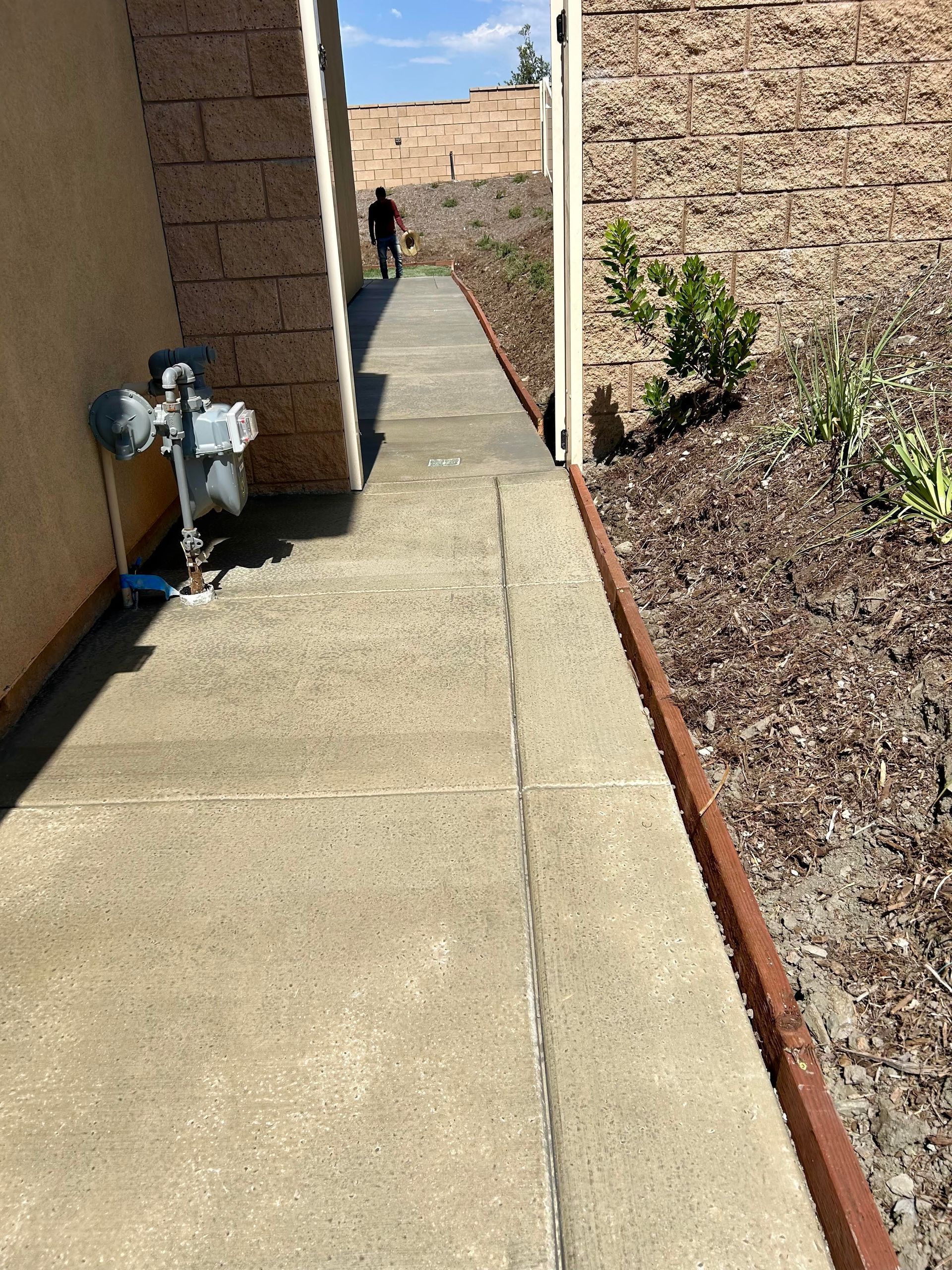 A person is walking down a sidewalk next to a brick wall.