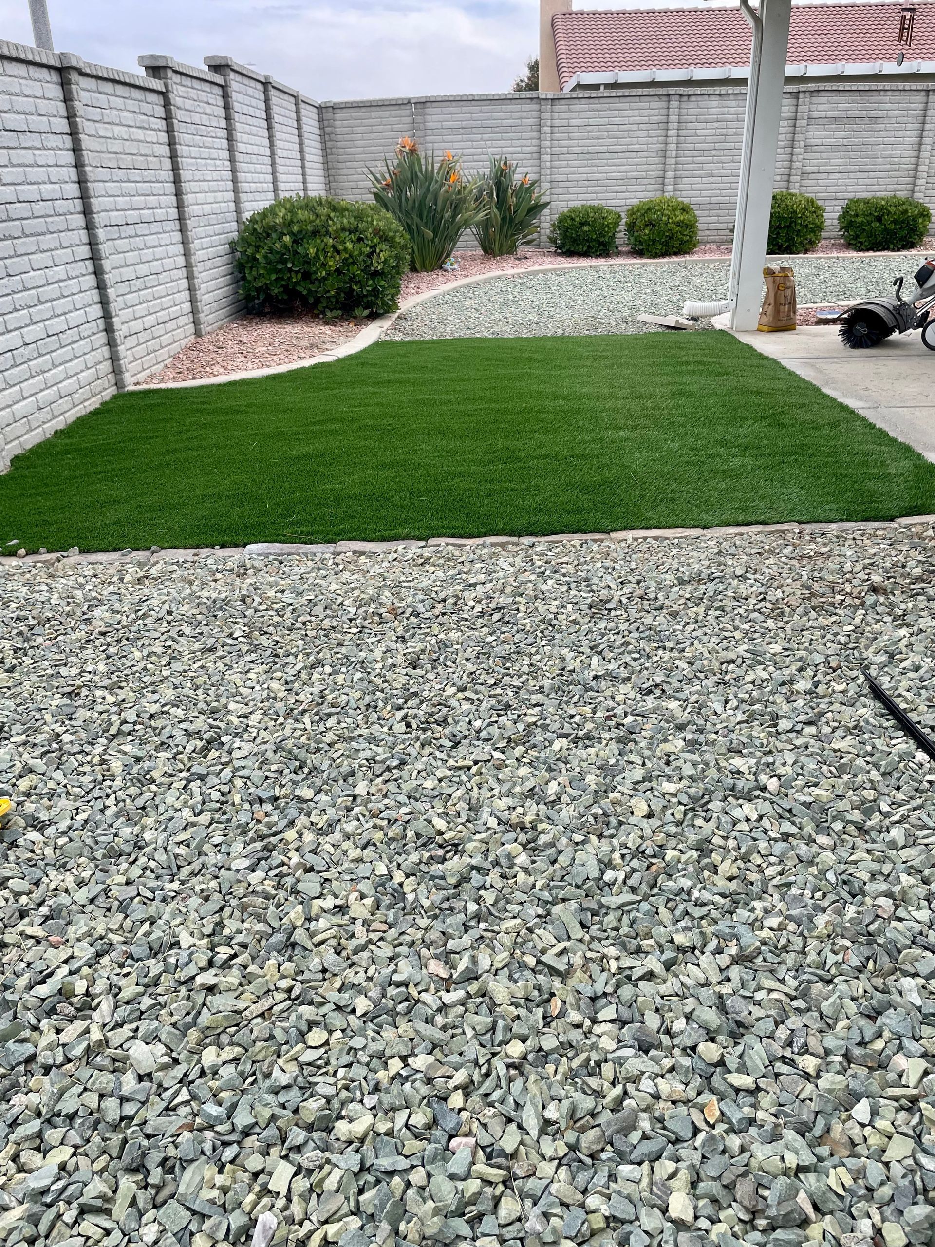 Backyard with gravel foreground, green lawn, raised planter, and white brick walls.