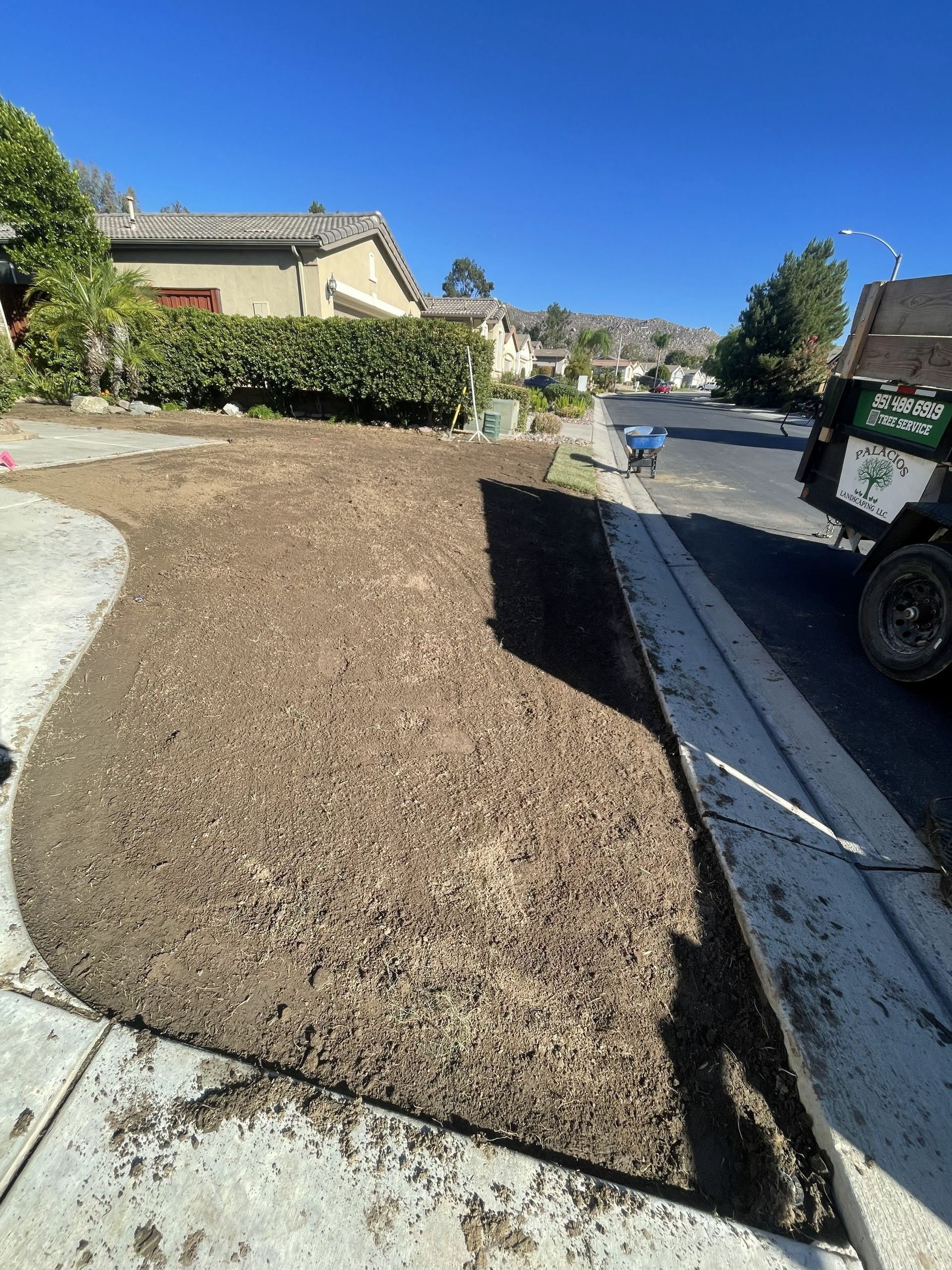 Front yard landscaping with brown dirt beside a driveway and parked truck on a sunny suburban street