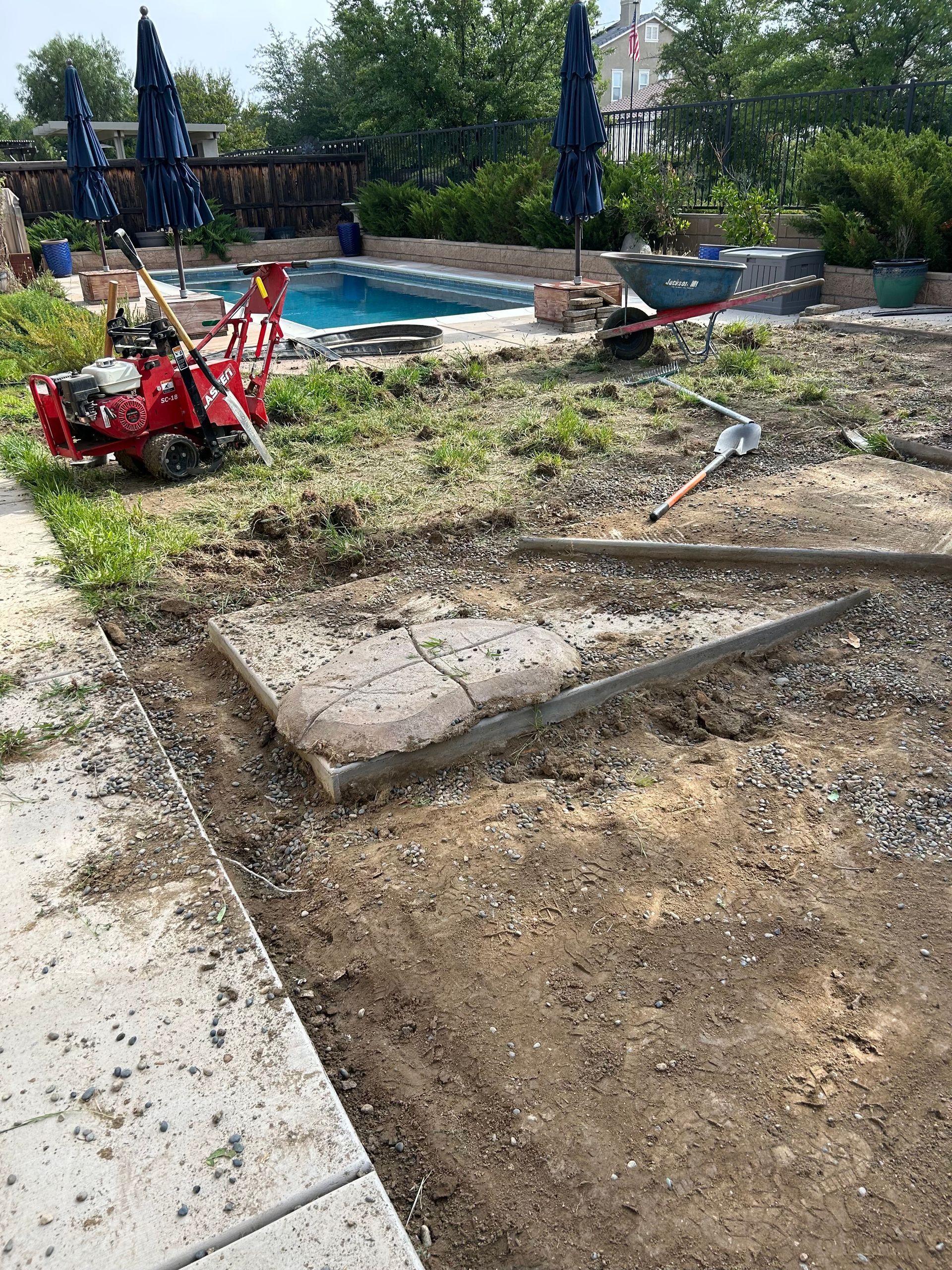 Backyard with grass and weeds being removed, tools and a pool in view