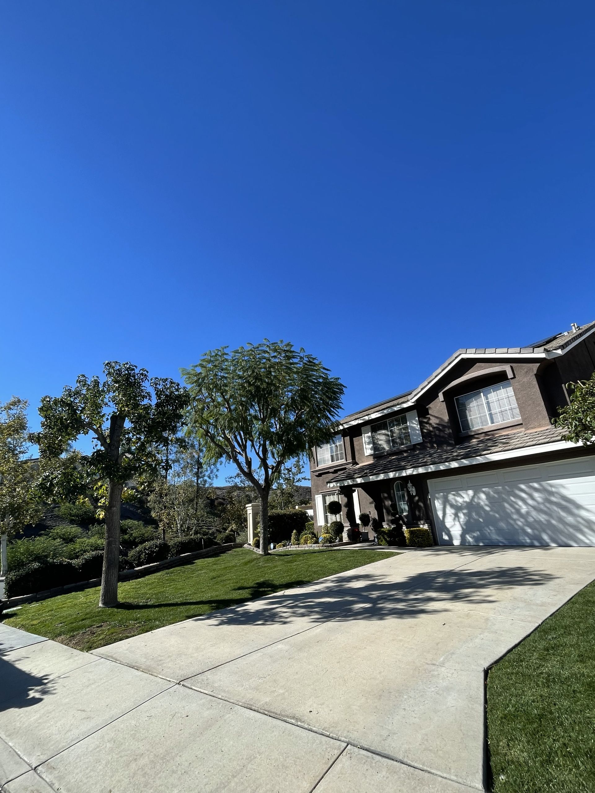Suburban house with white garage, curved driveway, and trees under a clear blue sky