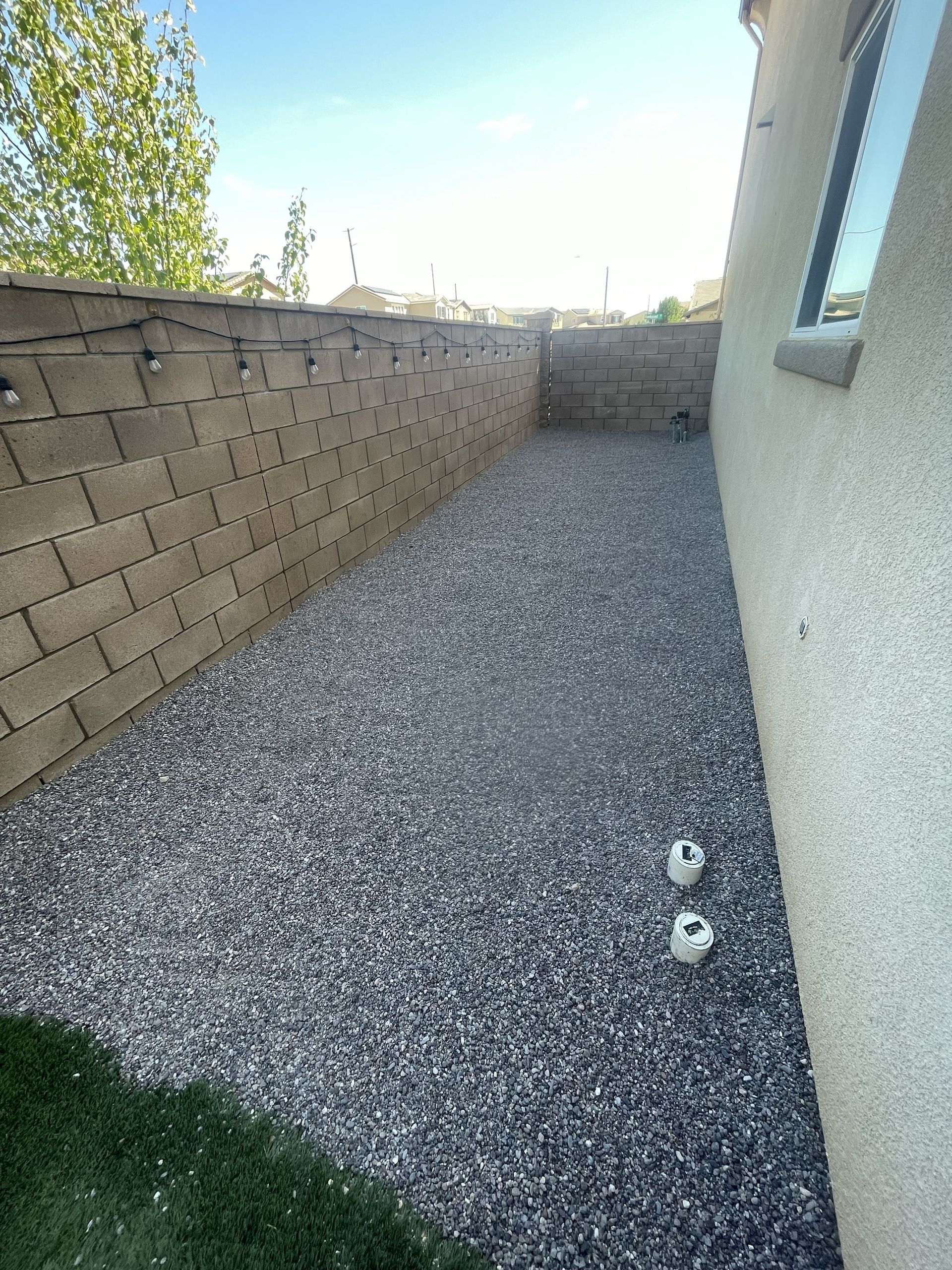 Narrow pea gravel side yard beside a house with a tan block wall and small window.