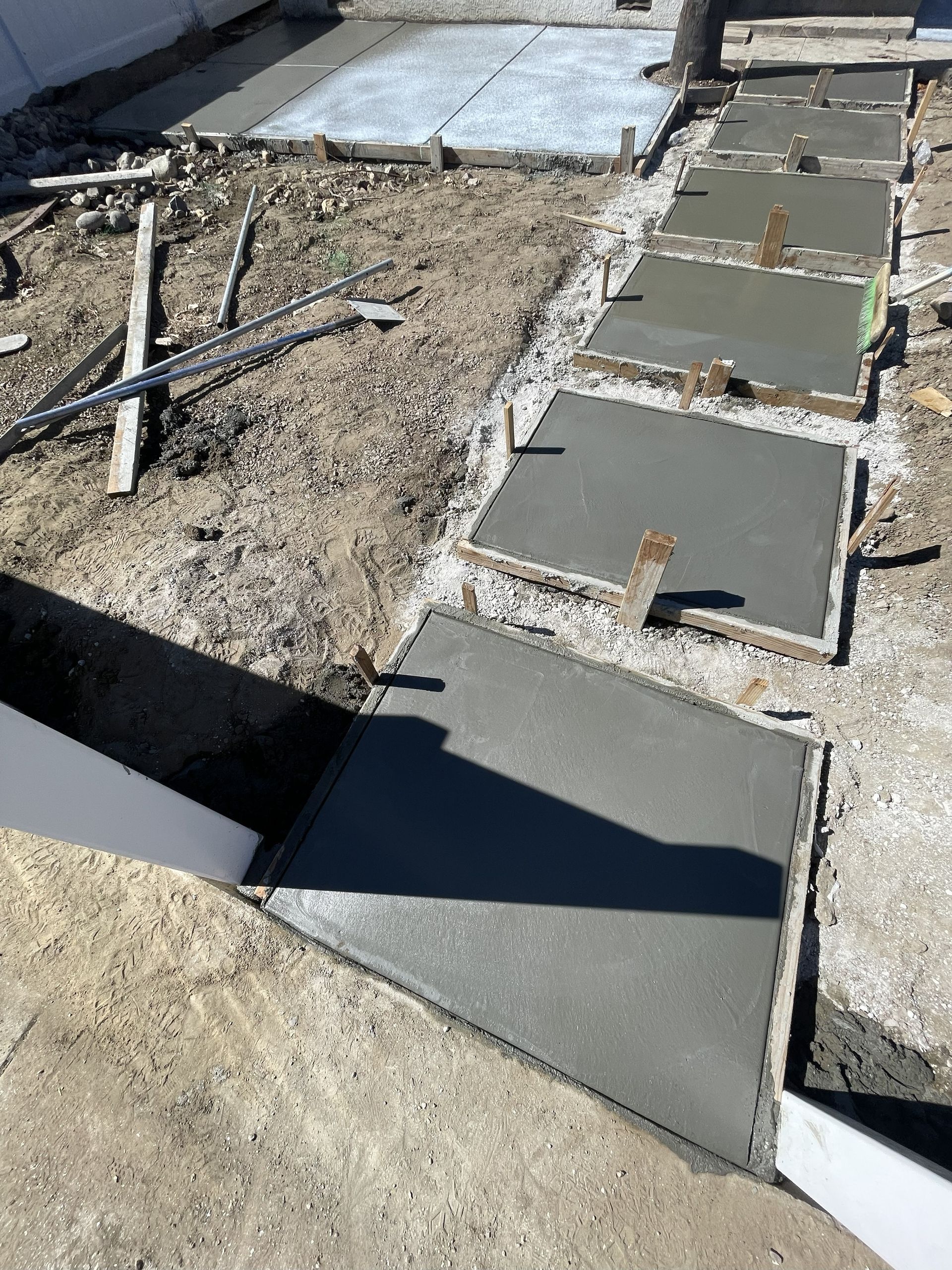 Partially paved walkway under construction with wet concrete slabs and gravel beside it
