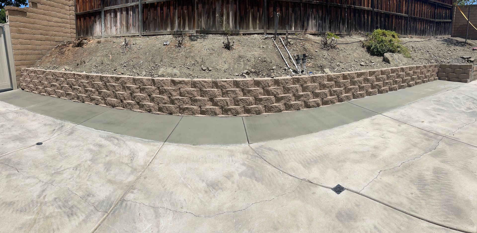 Concrete driveway with a stone retaining wall and wooden fence in a backyard