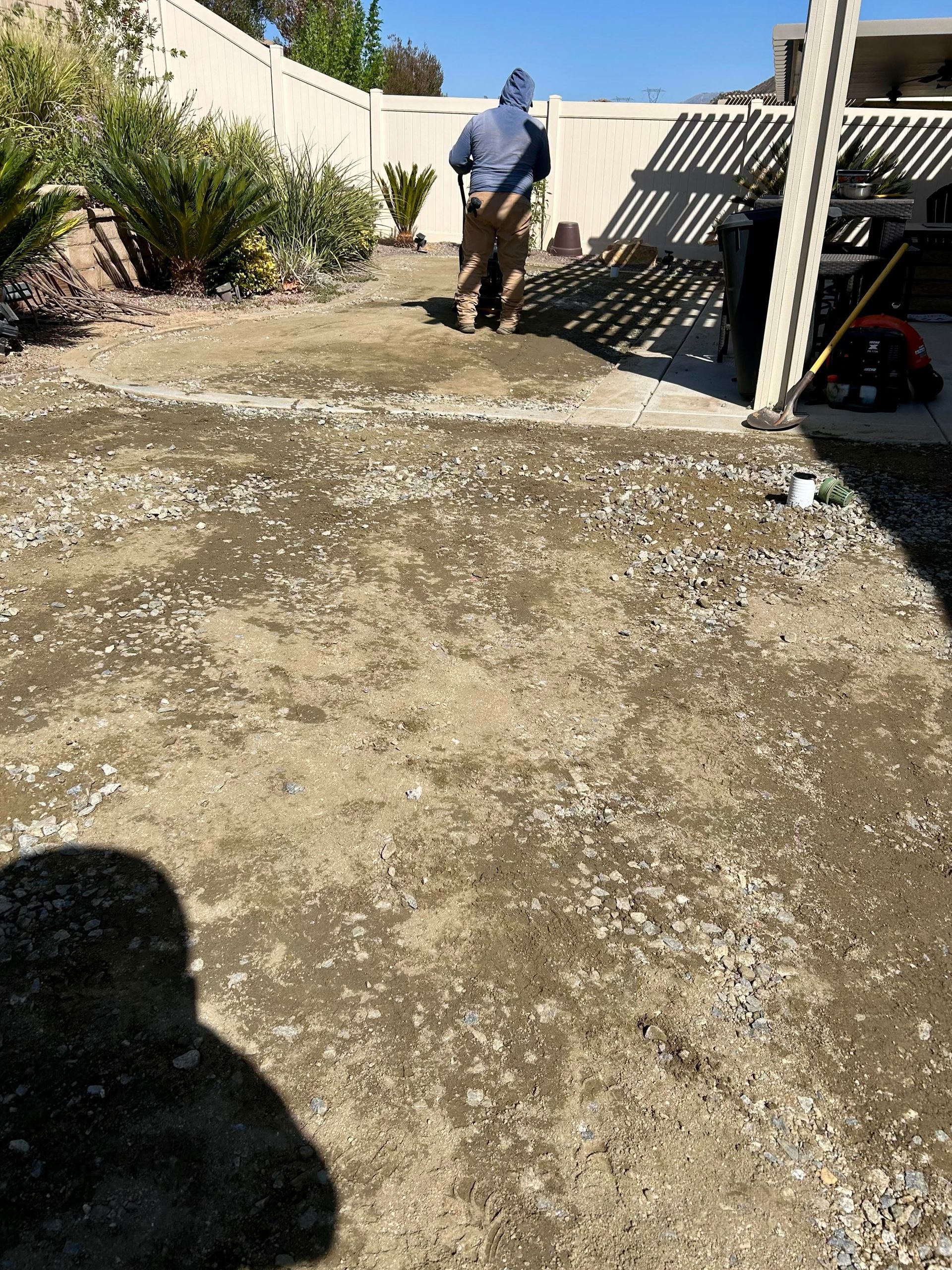 A man is shoveling dirt in a backyard.