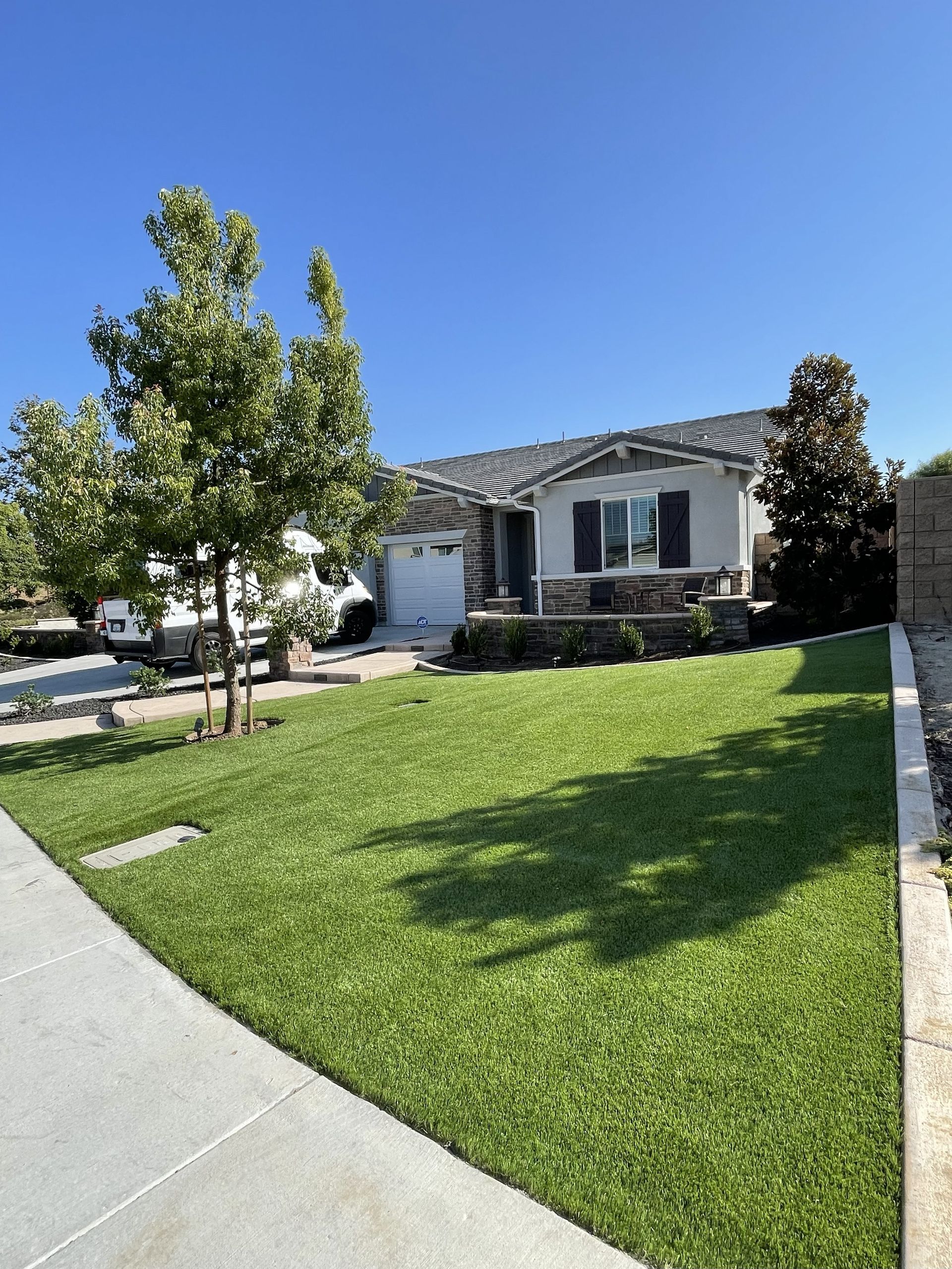 Suburban house with a manicured green lawn, trees, and a clear blue sky