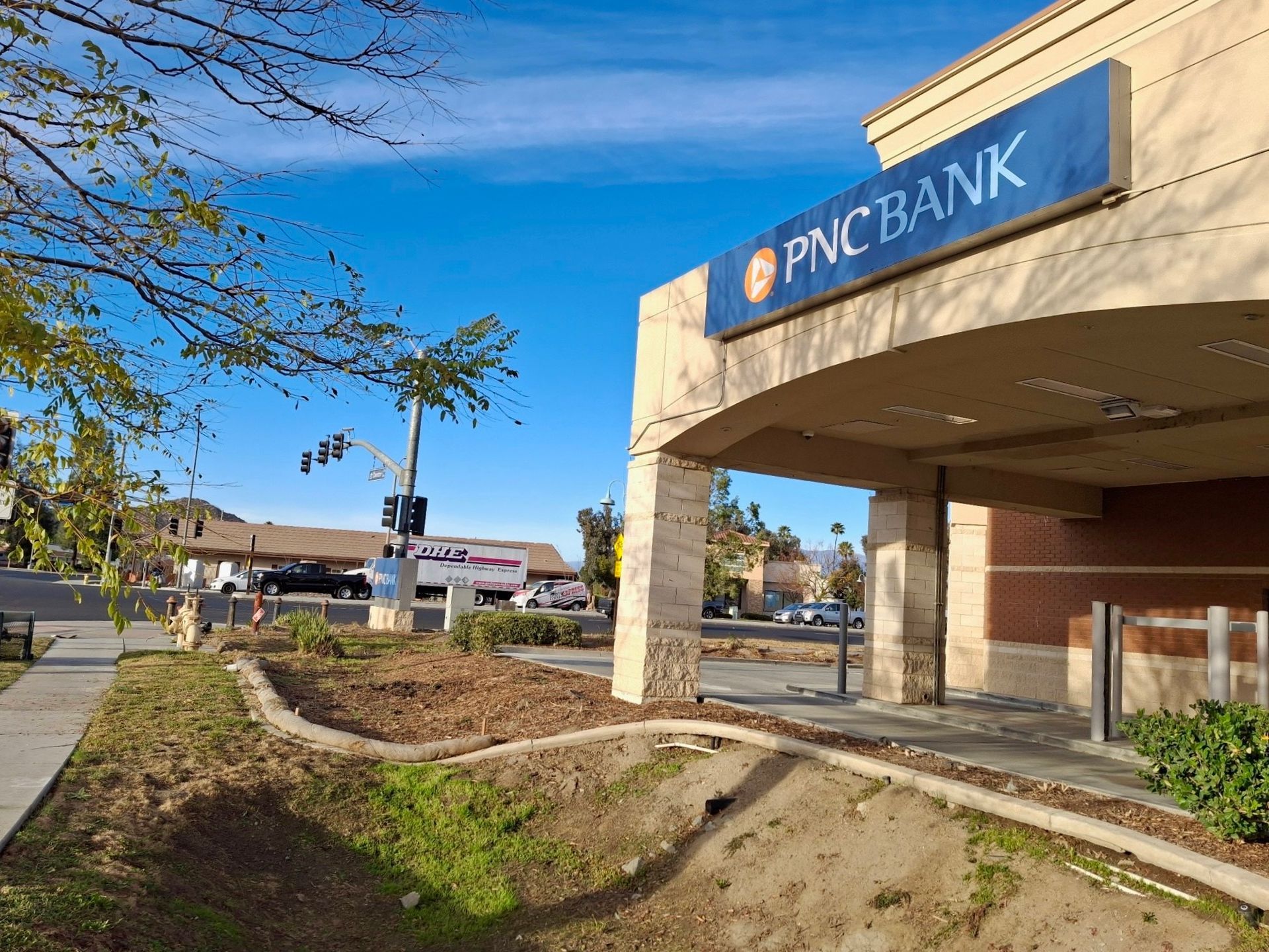 DNC Bank branch exterior with blue sign, drive-thru canopy, and sidewalk on a sunny day