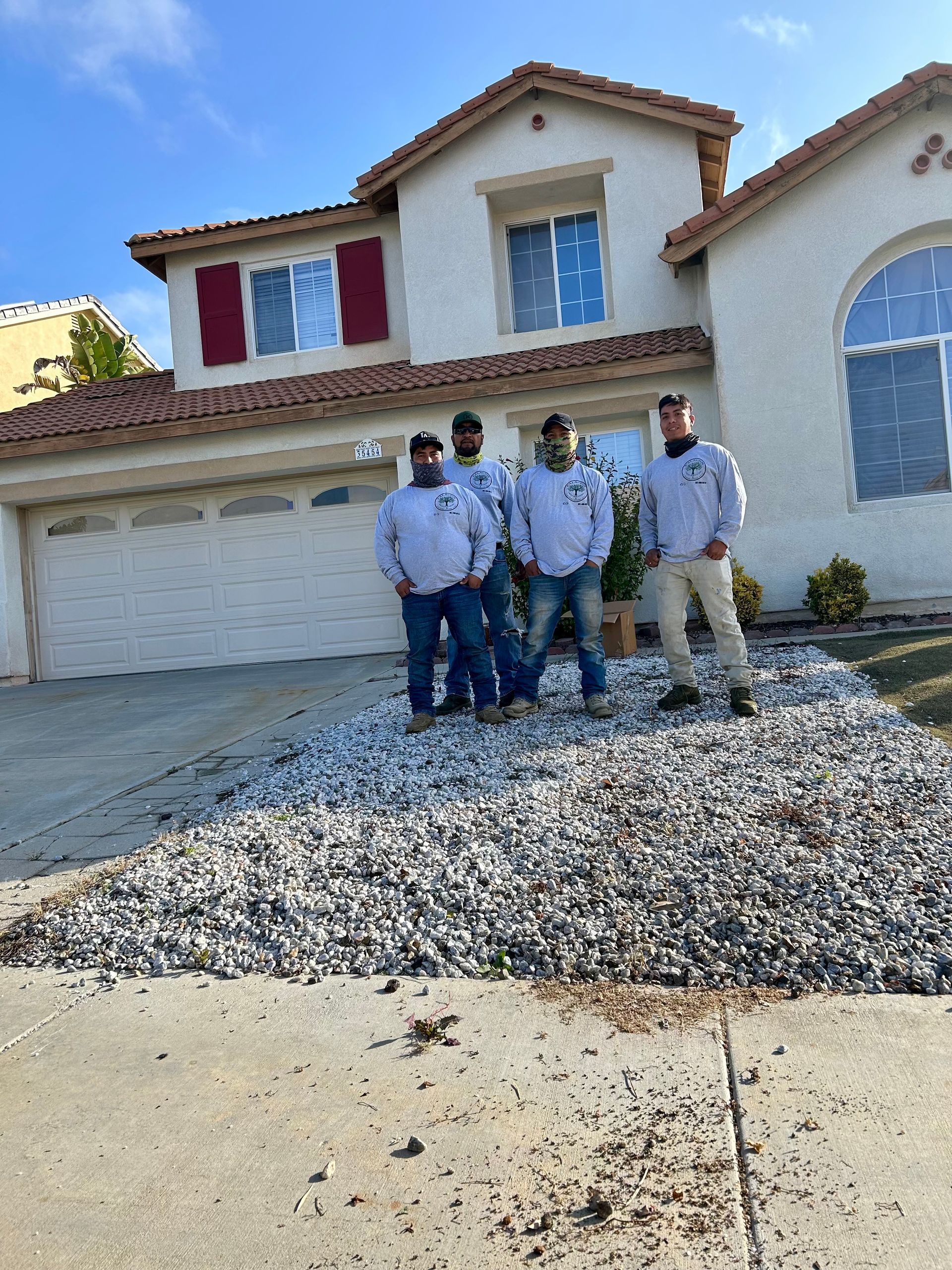 Four workers standing in front of a two-story house under construction, with gravel in the front yard