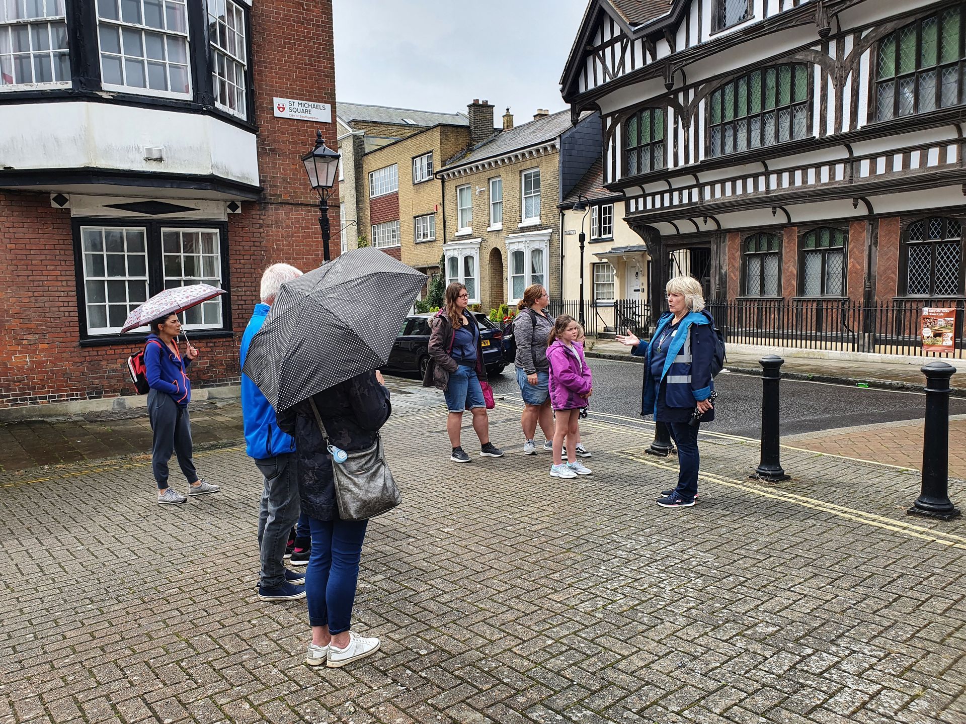 A group of people are standing on a cobblestone street holding umbrellas.