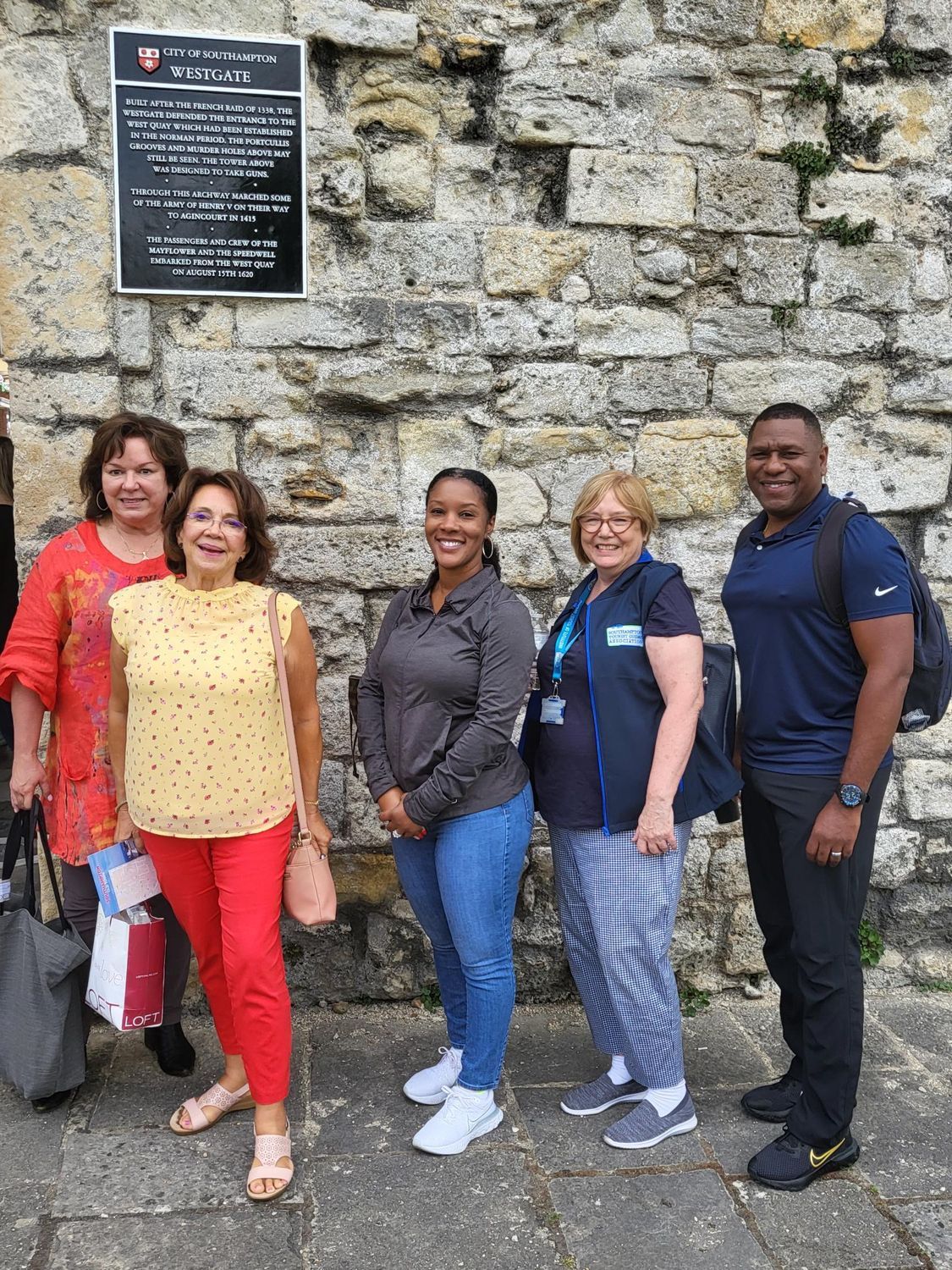 A group of people are standing in front of a stone wall.