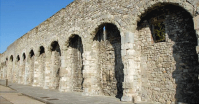 A stone wall with arches on it and a blue sky in the background