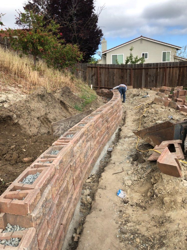 A man is working on a brick wall in a backyard.
