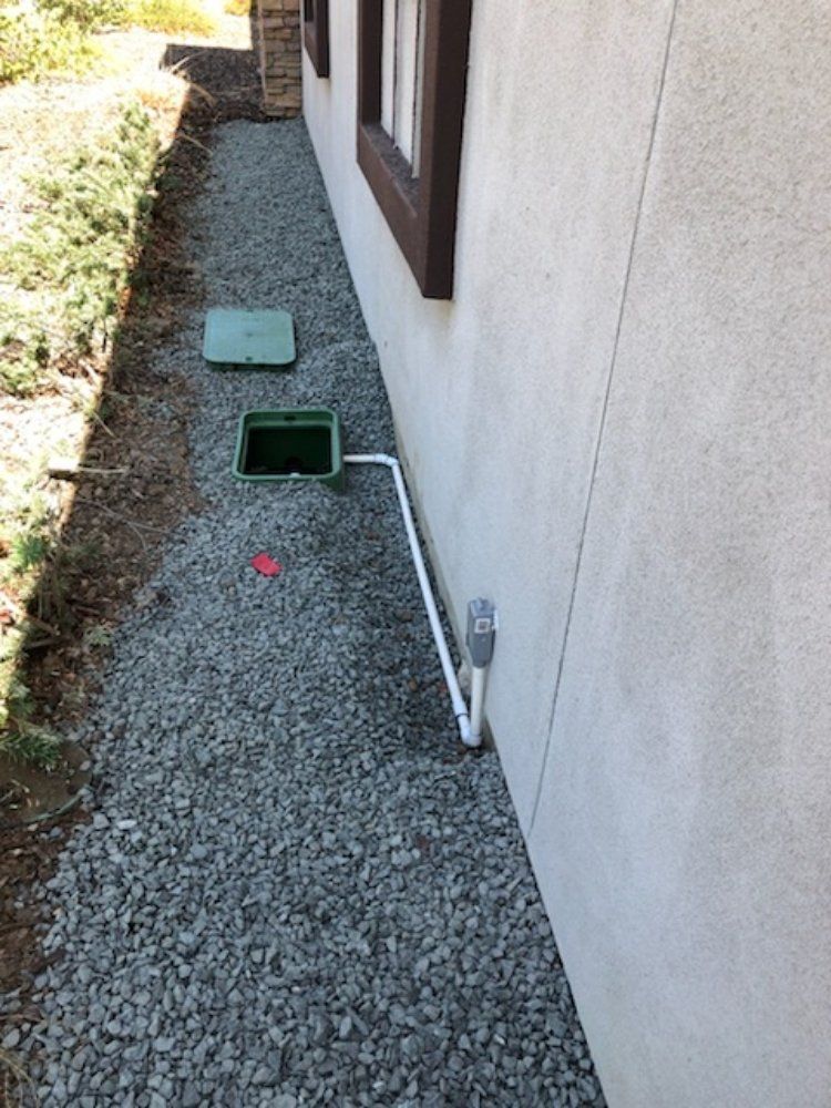 A pipe is connected to a green box on the side of a house.
