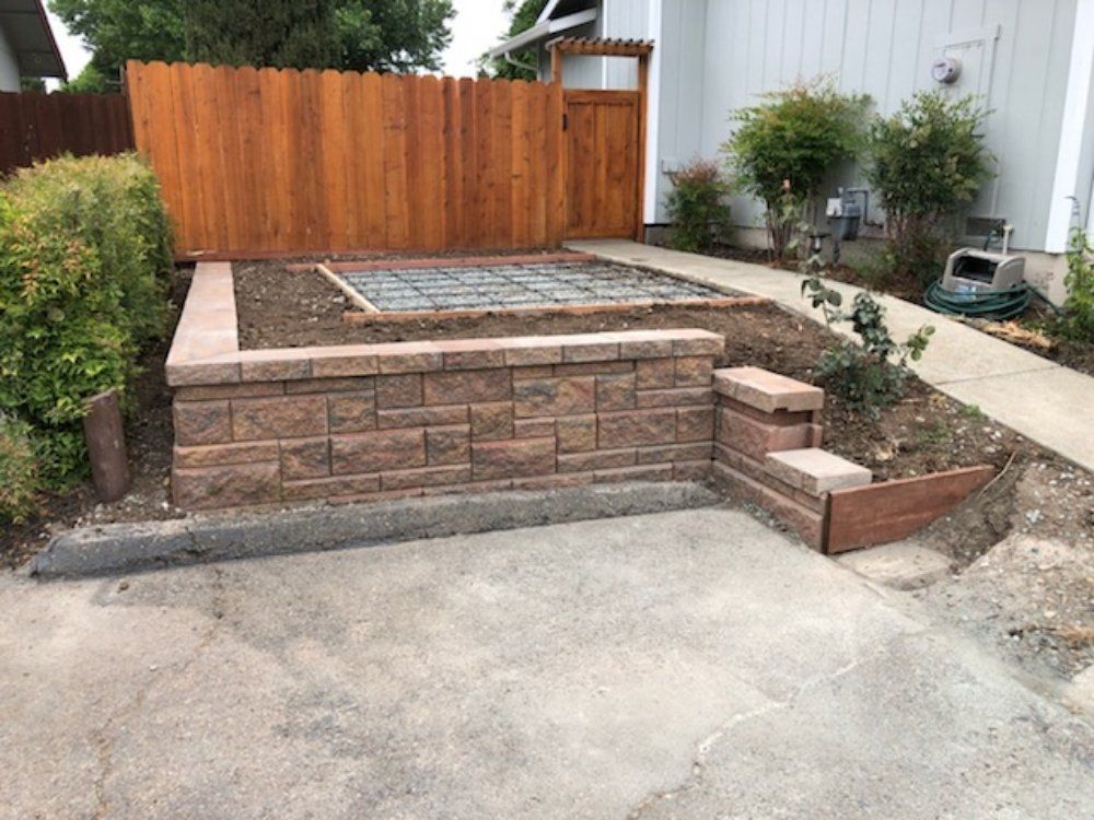 A brick wall is being built in front of a house with a wooden fence.