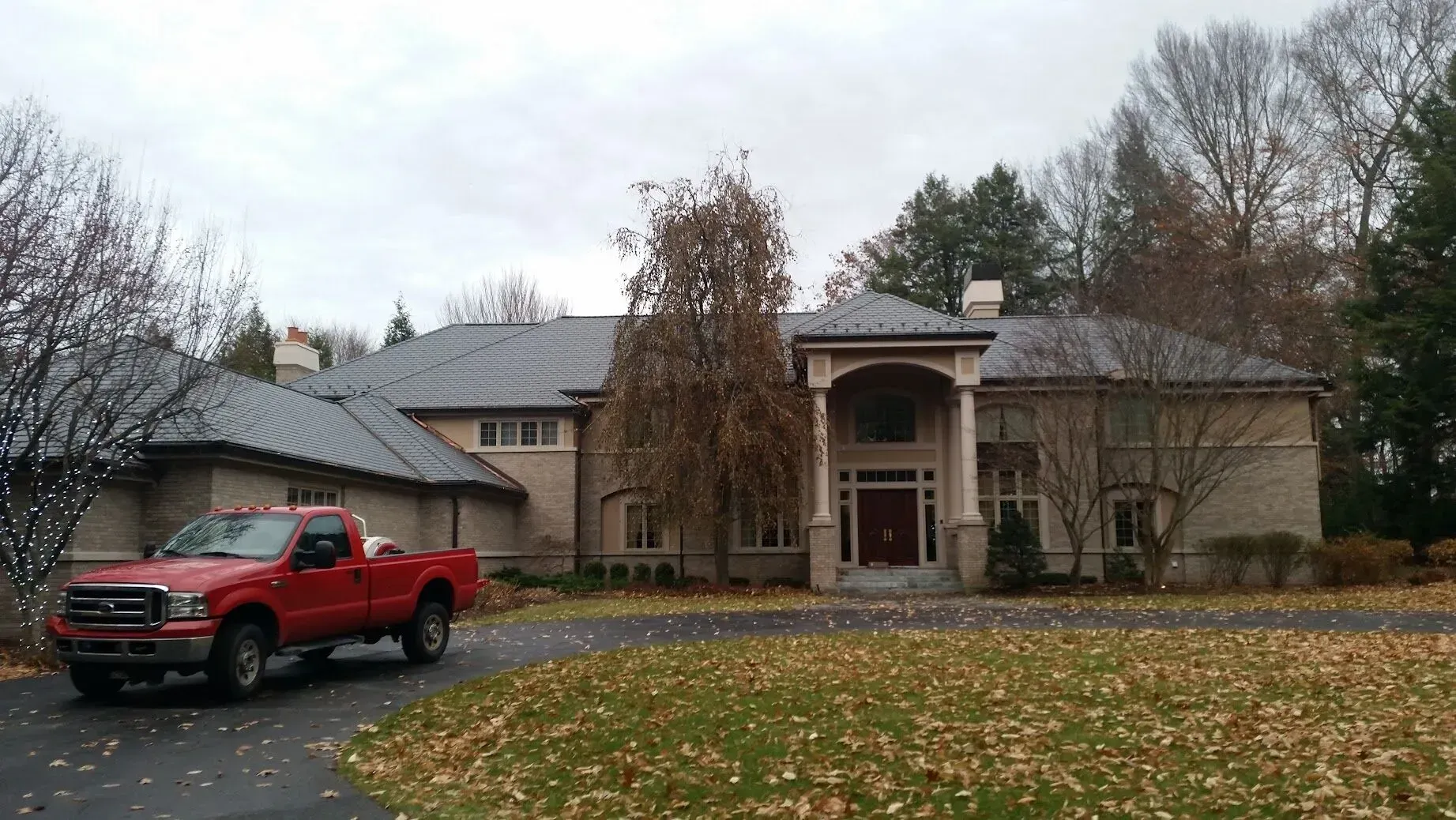 Red pickup truck parked in front of a house with a porch, surrounded by autumn trees and fallen leaves.