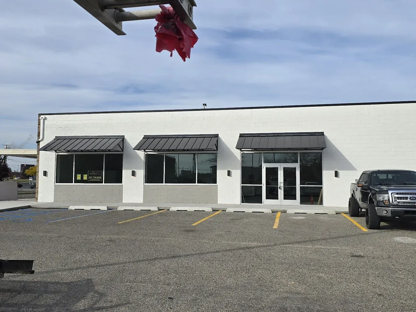 White storefront with black awnings and parked SUV on a gravel lot under cloudy sky