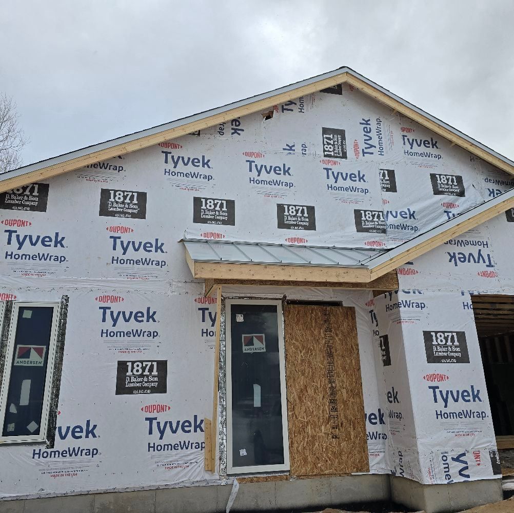 Partially built house wrapped in Tyvek with unfinished siding, windows, and a cloudy sky overhead