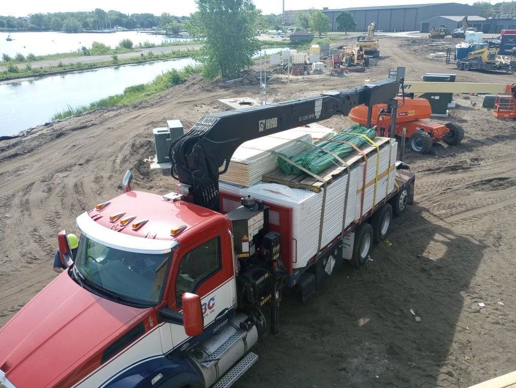 Red semi-truck with crane loading materials at a construction site by a waterway