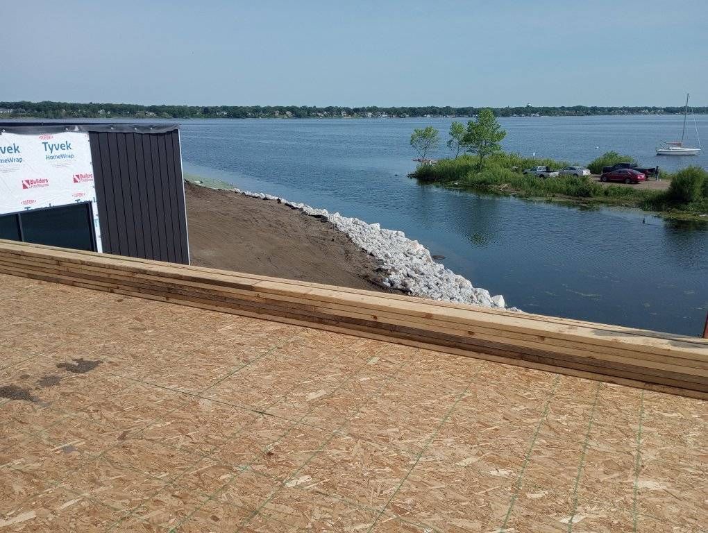 Riverside view from a wooden deck, with calm water, shoreline rocks, and a small green island under a cloudy sky