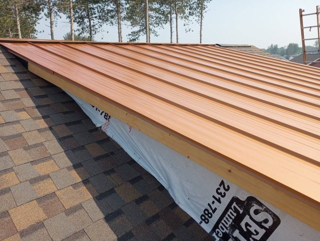 Copper-colored metal roof installation over brown shingles on a house rooftop
