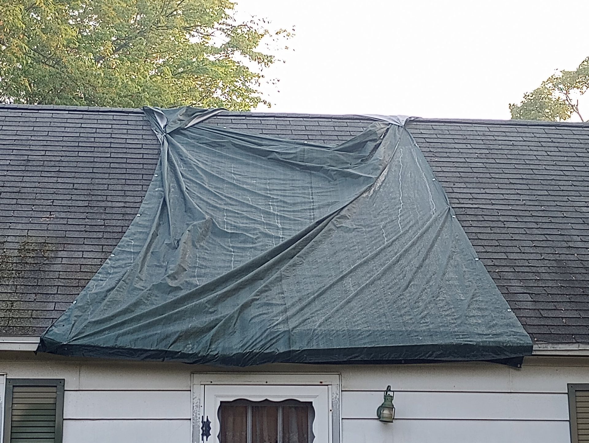Blue tarp covering part of a house roof after storm damage